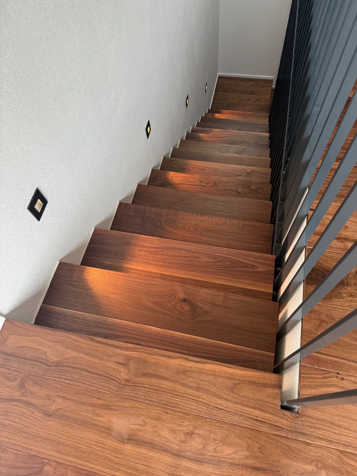 Dunkel gebeizte Holztreppe mit warmen seitlichen Stufenleuchten