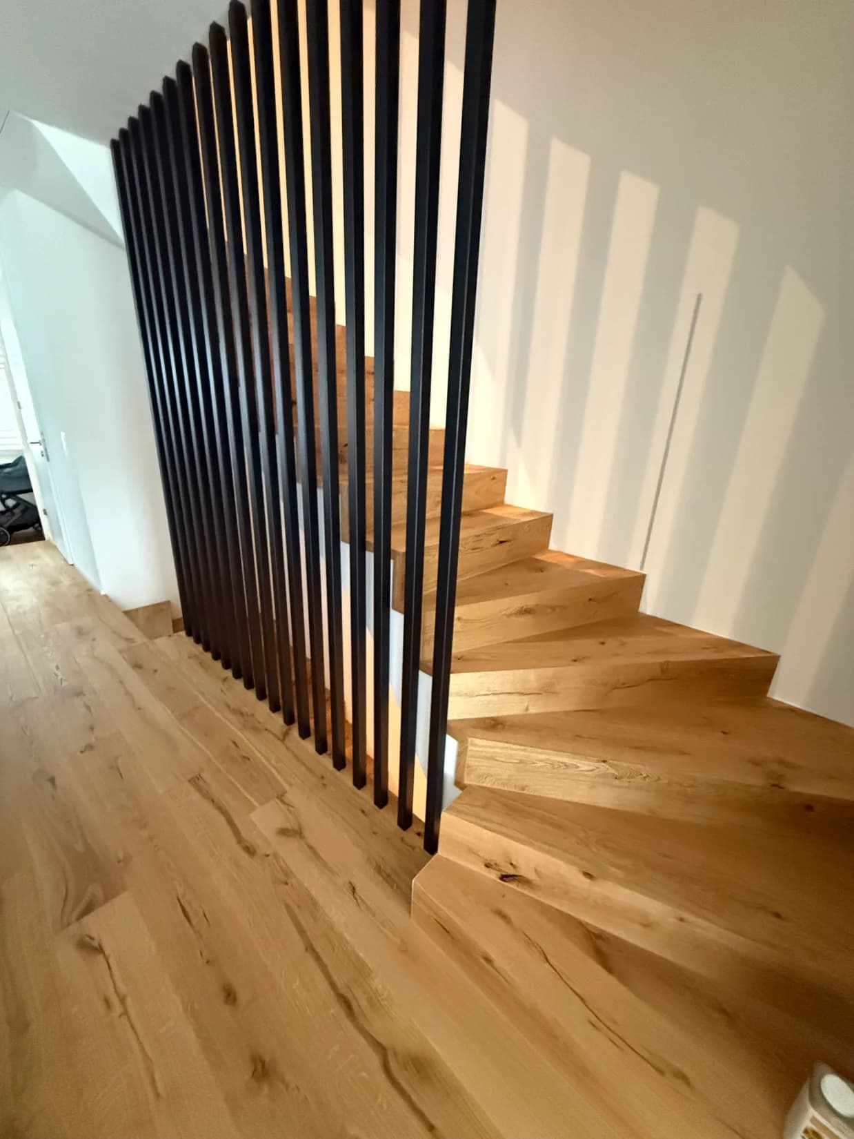 Eichentreppe mit raumhohen dunklen Holzlamellen als Geländer