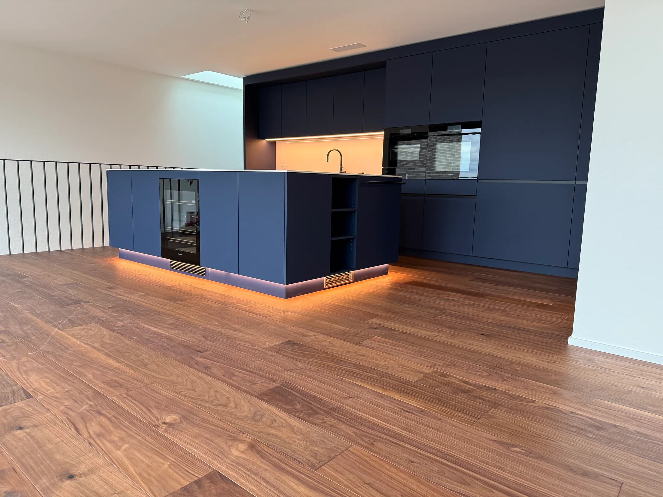 Offene blaue Küche mit dunkel getöntem Holzboden und beleuchtetem Sockel